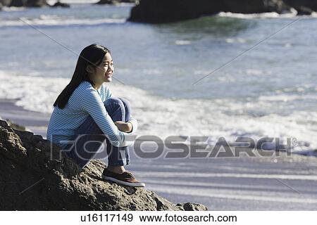 Stock Photo - Teenage girl sitting on coastal rock. Fotosearch