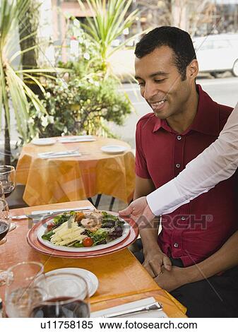 Waiter serving food to man in restaurant View Large Photo Image Stock Photography - Waiter serving food to man in restaurant. Fotosearch