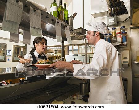 Picture - Waitress gesturing to chef in restaurant kitchen. Fotosearch