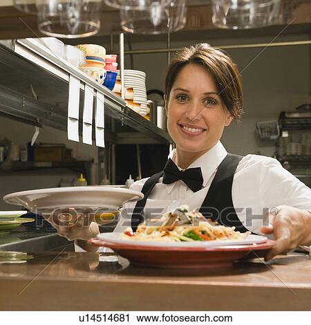 Stock Image - Waitress taking plates of food from kitchen. Fotosearch