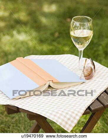 Stock Photo - Wine glass and book on outdoor table. Fotosearch