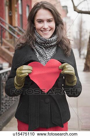 Stock Image - Woman holding heart cutout on urban street. Fotosearch