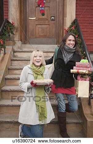 Picture - Women carrying Christmas gifts on front stoop. Fotosearch