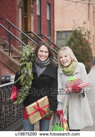 Stock Image - Women carrying Christmas gifts on urban street. Fotosearch