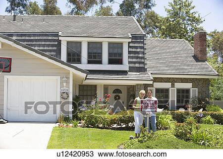 Couple Standing Outside House With Real Estate Sign View Large Photo Image Stock Image - Couple Standing Outside House With Real Estate Sign. Fotosearch