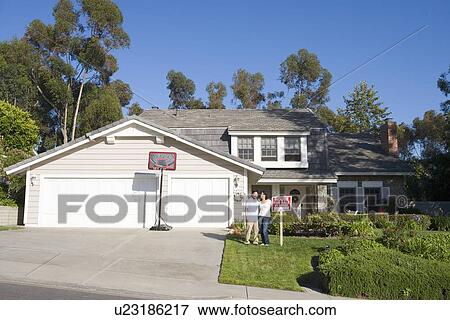 Couple Standing Outside House With Real Estate Sign View Large Photo Image Stock Photo - Couple Standing Outside House With Real Estate Sign. Fotosearch