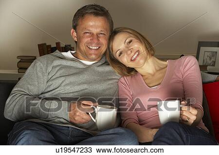 Stock Image - Couple With Coffee Mugs Watching Television. Fotosearch