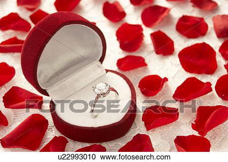 Stock Image - Diamond Ring In Heart Shaped Box Surrounded By Rose Petals. Fotosearch