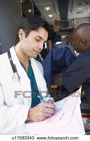 Stock Image - Doctor taking notes as paramedics unload patient. Fotosearch