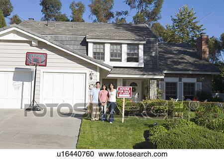 Stock Image - Family Standing Outside House With Real Estate Sign. Fotosearch