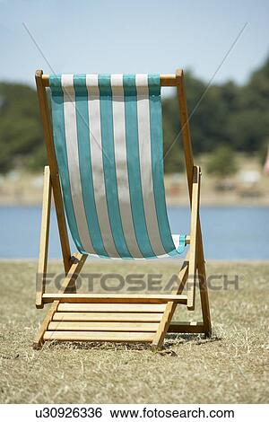 Stock Photograph - Lone Beach Chair Sitting Next To Water. Fotosearch