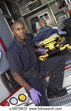 Stock Image - Male paramedic preparing to unload patient from ambulance. Fotosearch
