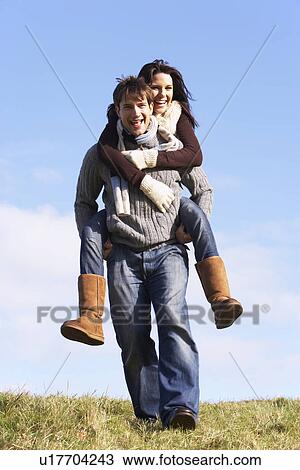 Stock Image - Man Giving His Wife A Piggy Back Ride In Park. Fotosearch