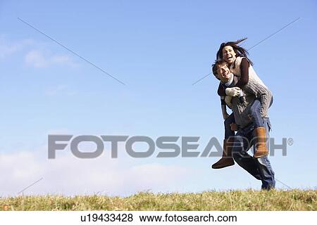 Stock Photo - Man Giving His Wife A Piggy Back Ride In Park. Fotosearch