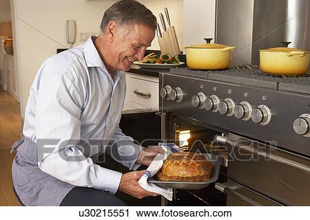 Stock Image - Man Taking Food Out Of The Oven. Fotosearch