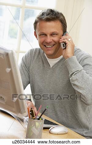 Picture - Man Using Computer And Talking On Phone. Fotosearch