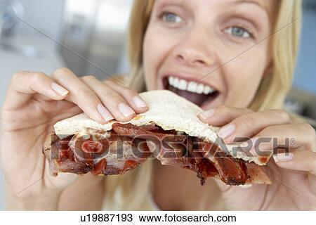 Stock Image - Mid Adult Woman Eating Bacon Sandwich. Fotosearch