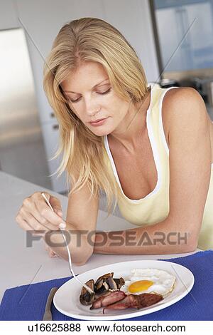 Stock Photo - Mid Adult Woman Eating Unhealthy Breakfast. Fotosearch