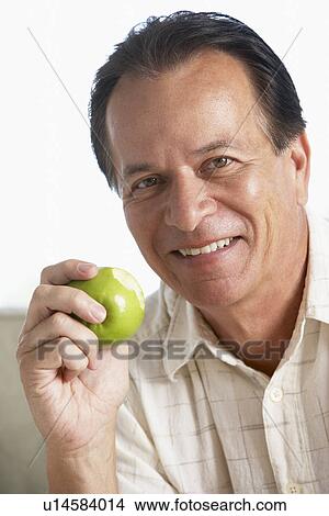 Picture - Middle Aged Man Eating Green Apple And Smiling At The Camera. Fotosearch