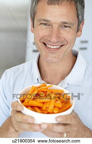 Picture - Middle Aged Man Holding A Bowl Of Carrots. Fotosearch