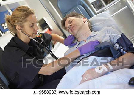 Stock Image - Paramedic attending to patient in ambulance. Fotosearch