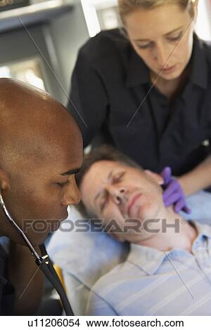 Picture - Paramedic using stethoscope on patient in ambulance. Fotosearch