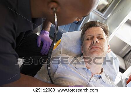 Stock Image - Paramedic using stethoscope on patient in ambulance. Fotosearch