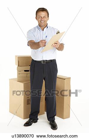 Stock Image - Portrait Of Courier Standing Next To Parcels, Holding A Clipboard. Fotosearch