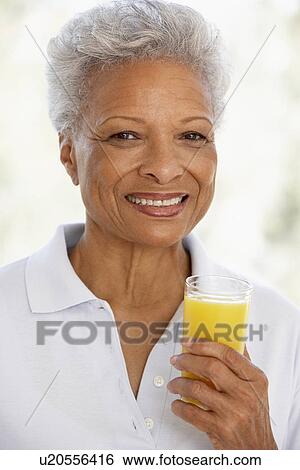 Stock Photograph - Senior Adult Holding A Glass Of Fresh Orange Juice, Smiling At The Camera. Fotosearch
