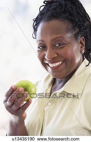 Stock Image - Senior Woman Eating Green Apple And Smiling At The Camera. Fotosearch