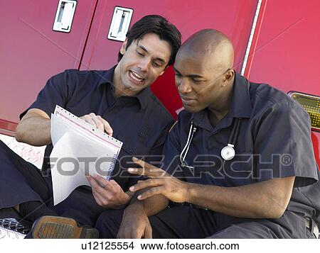Two paramedics cheerfully doing paperwork, sitting by their ambulance View Large Photo Image Picture - Two paramedics cheerfully doing paperwork, sitting by their ambulance. Fotosearch