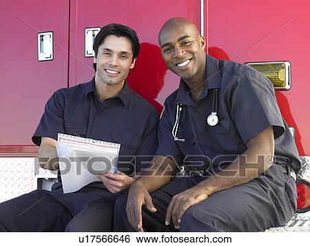 Stock Photograph - Two paramedics cheerfully doing paperwork, sitting by their ambulance. Fotosearch