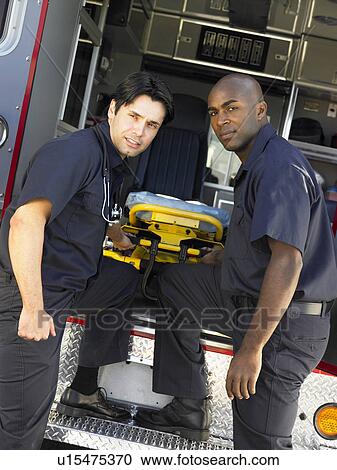 Stock Image - Two paramedics cheerfully removing empty gurney from ambulance. Fotosearch