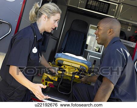 Stock Photograph - Two paramedics cheerfully removing empty gurney from ambulance. Fotosearch