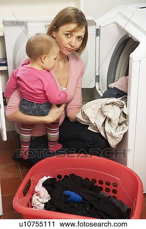 Stock Image - Woman Doing Laundry And Holding Baby Daughter. Fotosearch