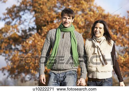 Stock Image - Young Couple Walking In Park Holding Hands. Fotosearch