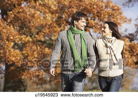 Stock Image - Young Couple Walking In Park Holding Hands. Fotosearch