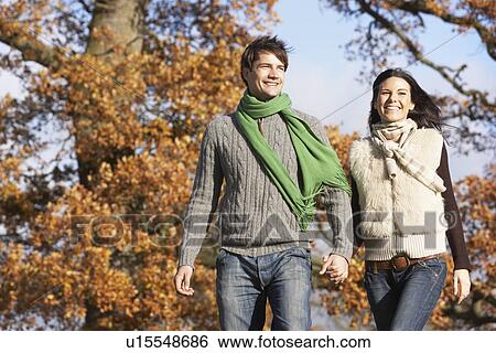 Stock Photograph - Young Couple Walking In Park Holding Hands. Fotosearch