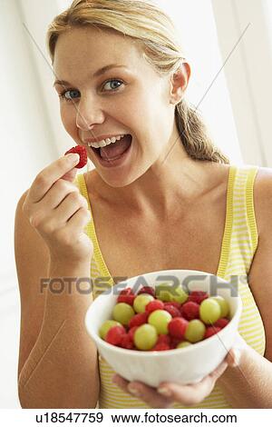 Stock Photo - Young Woman Eating A Bowl Of Fruit. Fotosearch