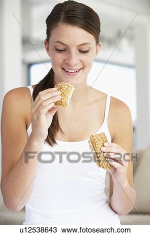 Stock Image - Young Woman Eating Brown Bread Roll. Fotosearch