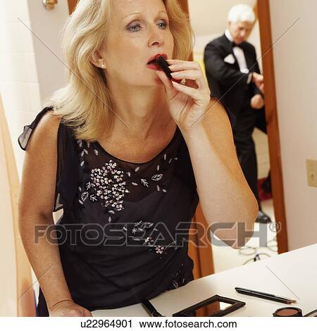 Close-up of a mature woman applying lipstick with a mature man standing in the background View Large Photo Image Stock Image - Close-up of a mature woman applying lipstick with a mature man standing in the background. Fotosearch
