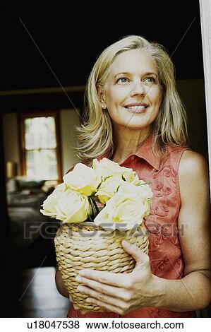 Close-up of a mature woman holding flowers in a vase and smiling View Large Photo Image Stock Photo - Close-up of a mature woman holding flowers in a vase and smiling. Fotosearch