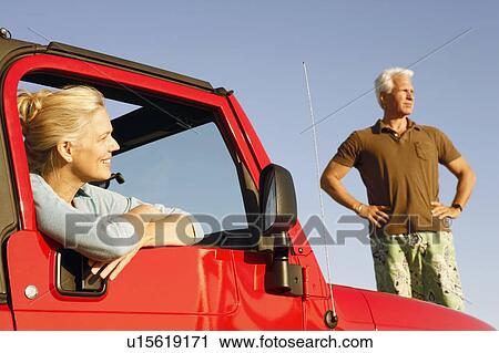 Stock Image - Close-up of a mature woman sitting in a sports utility vehicle with a mature man standing beside her. Fotosearch