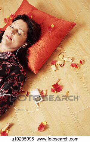 Stock Photography - High angle view of a mature woman lying on a wooden floor and listening to an MP3 player. Fotosearch