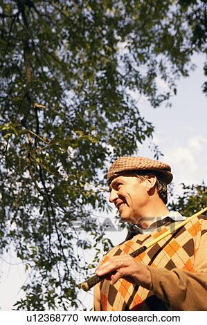 Stock Image - Low angle view of a mature man holding a golf club. Fotosearch