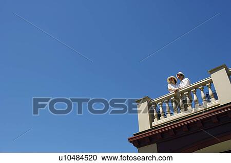 Stock Image - Low angle view of a mid adult couple standing on a terrace. Fotosearch