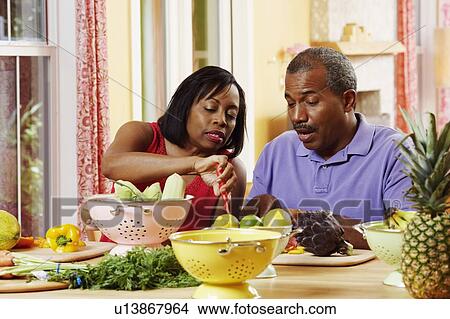 Picture - Mature couple cutting vegetables and talking. Fotosearch