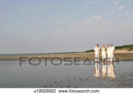 Stock Image - Mature couple standing with a mid adult woman and a mature man on the beach. Fotosearch