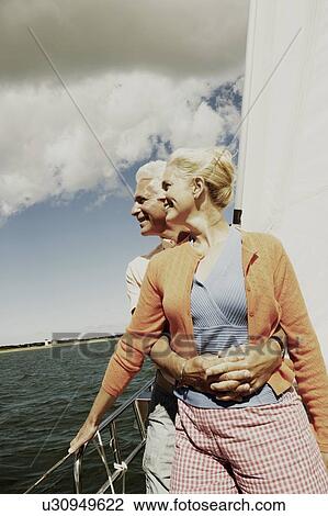 Stock Image - Mature man embracing a mature woman from behind in a sailboat and smiling. Fotosearch