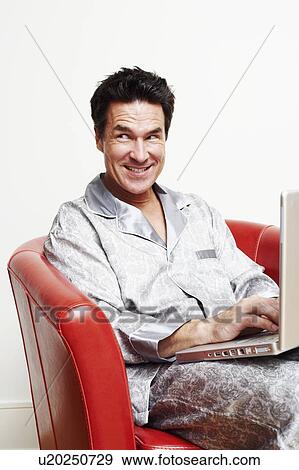 Mature man sitting in an armchair with a laptop and smiling View Large Photo Image Stock Photo - Mature man sitting in an armchair with a laptop and smiling. Fotosearch